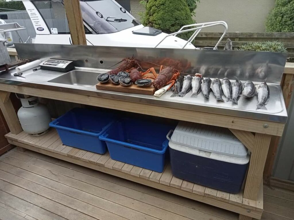 Long fish filleting bench loaded up with crays, blue code and paua after arriving back from a dive trip.