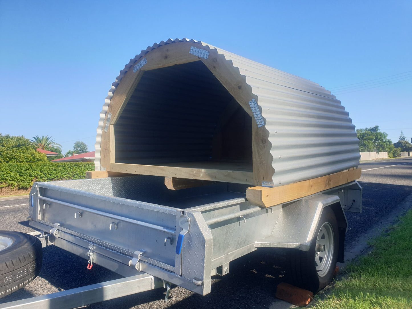 Animal shelter for sale in NZ | suitable for large dogs, pigs, lambs and calves | Round wooden shelter with corrugate iron roof, floor boards and back wall waiting for delivery on a single axle trailer | For sale in Auckland, Waikato and the North Island New Zeland